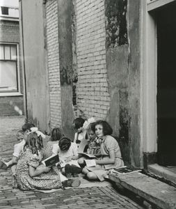 876881 Afbeelding van een groep kinderen, voornamelijk meisjes, zittend op een kleedje in de Korte Hamstraat in Wijk C ...